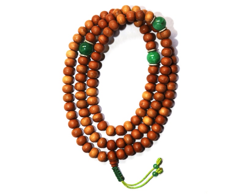 May include: A brown wooden mala bead necklace with green gemstone accents. The necklace is made of 108 beads and has a tassel at the end.