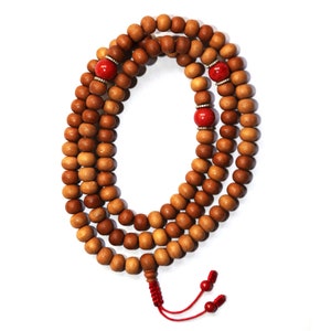 May include: A brown wooden mala bead necklace with red beads and a red tassel. The mala has 108 beads.