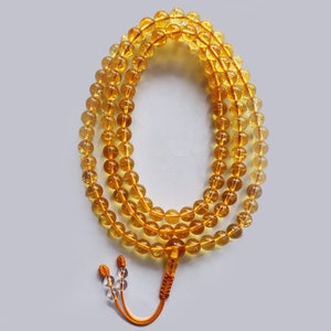 May include: A yellow citrine gemstone mala with a tassel. The mala is made of round beads and is strung on a cord.