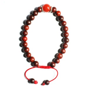 May include: A red wooden beaded bracelet with a red stone bead and silver accents. The bracelet is tied with a red cord.