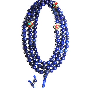 May include: A blue lapis lazuli mala prayer bead necklace with three decorative metal beads. The necklace is made of 108 beads and has a tassel at the end.
