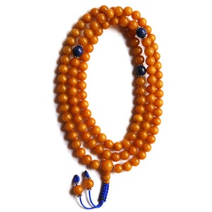 Op de afbeelding: Een gele amber mala kralenketting met blauwe lapis lazuli accent kralen en een blauwe kwast.
