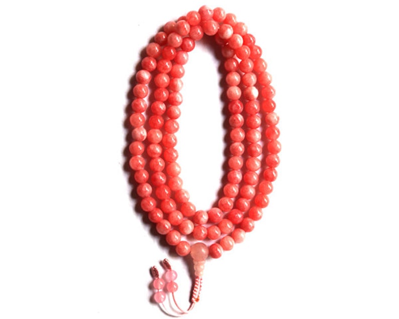 May include: A coral-colored beaded necklace with a tassel. The beads are round and smooth, and the necklace is strung on a thin cord.