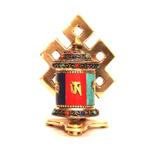 May include: A gold prayer wheel with a colorful design and intricate details. The wheel is mounted on a stand with a decorative knot design.