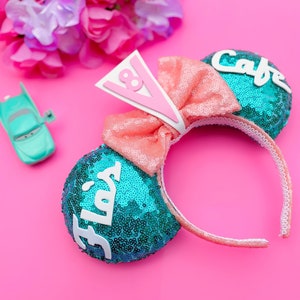May include: A pair of turquoise and pink sequined Minnie Mouse ears with a white bow and the words "Flo's Cafe" on them.