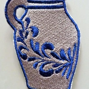Könnte beinhalten: Ein blauer und weißer gestickter Aufnäher einer Keramikkanne mit Blumenmuster.