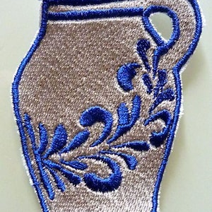 Puede incluir: Un parche de planchado beige bordado con un c&aacute;ntaro azul y blanco con un dise&ntilde;o floral.