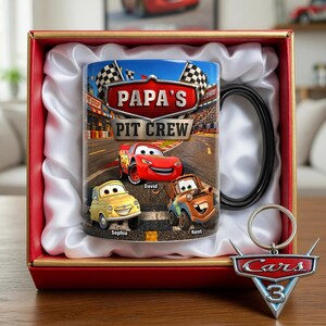 Puede incluir: Un juego de regalo tem&aacute;tico de Cars 3 en una caja roja, con una taza y un llavero. La taza tiene un asa negra y muestra el texto "Papa's Pit Crew" con coches de carreras de dibujos animados. El llavero es un logotipo de Cars 3.