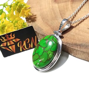 Puede incluir: Un collar de plata con un colgante ovalado de turquesa verde. La piedra tiene un patr&oacute;n de m&aacute;rmol y est&aacute; engastada en un bisel de plata.