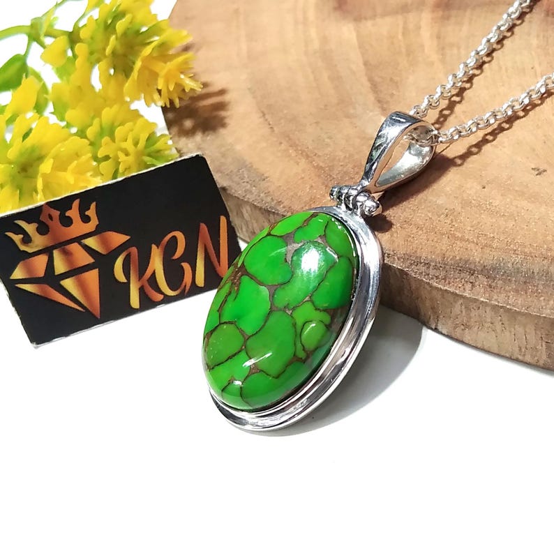 Puede incluir: Un collar de plata con un colgante ovalado de turquesa verde. La piedra tiene un patr&oacute;n de m&aacute;rmol y est&aacute; engastada en un bisel de plata.