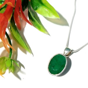 Puede incluir: Un collar de cadena de plata con un colgante que presenta una piedra preciosa verde oscura grande de forma ovalada.