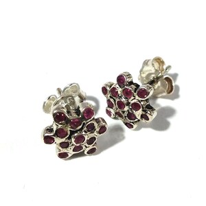 May include: A pair of silver stud earrings. Each earring has a cluster of small, round, deep red gemstones set in silver metal. The earrings are shown against a white background.