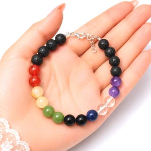 Può includere: Un braccialetto di perline con elementi rotondi di vari colori e consistenze, tra cui perle di pietra lavica nera porosa, perle di vetro lisce rosse, gialle, verdi, blu, viola e trasparenti, rifinito con una chiusura a moschettone argentata.