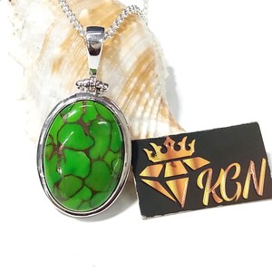 Puede incluir: Un collar de cadena de plata con un colgante ovalado verde con una piedra turquesa con vetas marrones. El colgante est&aacute; engastado en un bisel de plata.