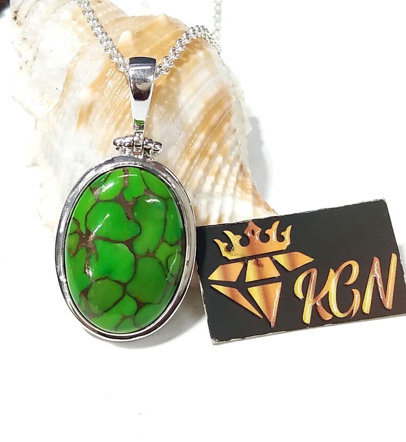 Puede incluir: Un collar de cadena de plata con un colgante ovalado verde con una piedra turquesa con vetas marrones. El colgante est&aacute; engastado en un bisel de plata.