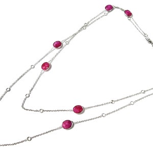 Op de afbeelding: Een lange zilverkleurige ketting met meerdere ovaalvormige, gefacetteerde dieproze stenen die gelijkmatig over de schakels zijn verdeeld. De ketting is in een dubbele lus gerangschikt en toont een zilveren afwerking met levendige roze edelsteenaccenten.