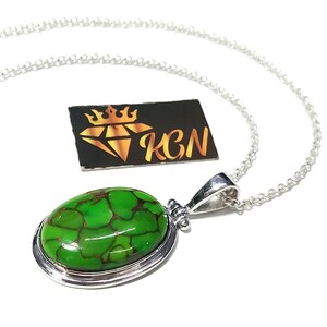 Puede incluir: Un collar de cadena de plata con un colgante ovalado verde con una piedra turquesa. El colgante tiene un borde de plata y una argolla de plata.