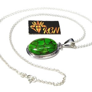 Puede incluir: Un collar de cadena de plata con un colgante ovalado verde con una piedra turquesa. El colgante tiene un engaste de bisel de plata y una argolla de plata.