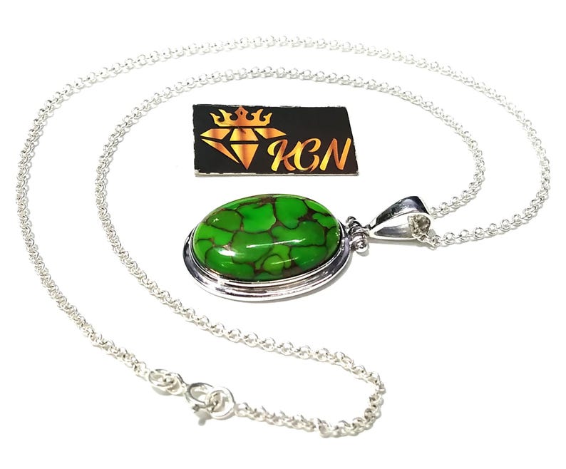 Puede incluir: Un collar de cadena de plata con un colgante ovalado verde con una piedra turquesa. El colgante tiene un engaste de bisel de plata y una argolla de plata.