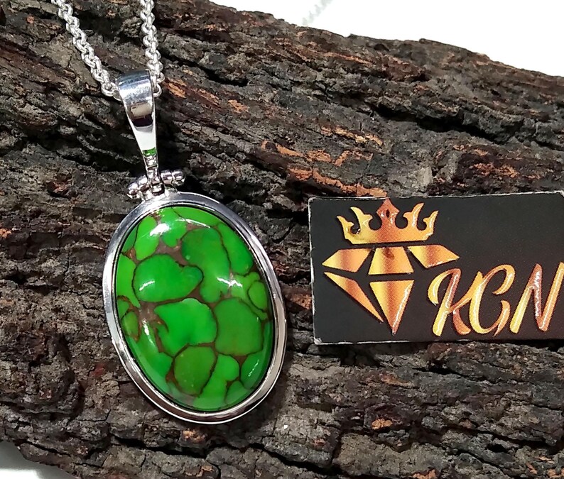 Puede incluir: Un collar con un colgante de plata con una piedra ovalada de turquesa verde. La piedra tiene un patr&oacute;n de m&aacute;rmol y est&aacute; engastada en un bisel de plata.