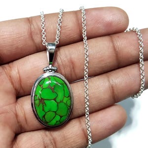 Puede incluir: Un collar de cadena de plata con un colgante ovalado verde con una piedra turquesa. La piedra tiene un patr&oacute;n de m&aacute;rmol con matices verdes y marrones.