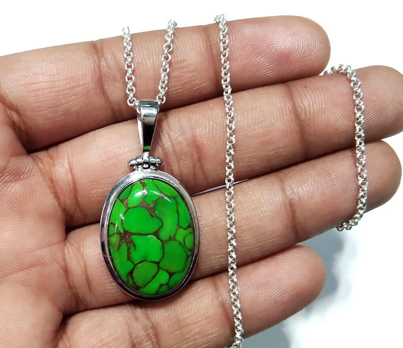 Puede incluir: Un collar de cadena de plata con un colgante ovalado verde con una piedra turquesa. La piedra tiene un patr&oacute;n de m&aacute;rmol con matices verdes y marrones.