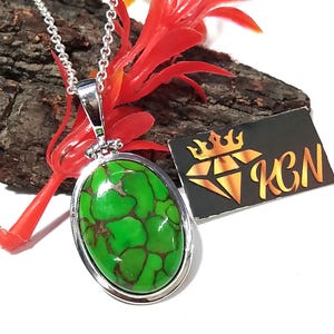 Puede incluir: Un collar de cadena de plata con un colgante ovalado con una piedra turquesa verde y marr&oacute;n. El colgante tiene un borde de plata.