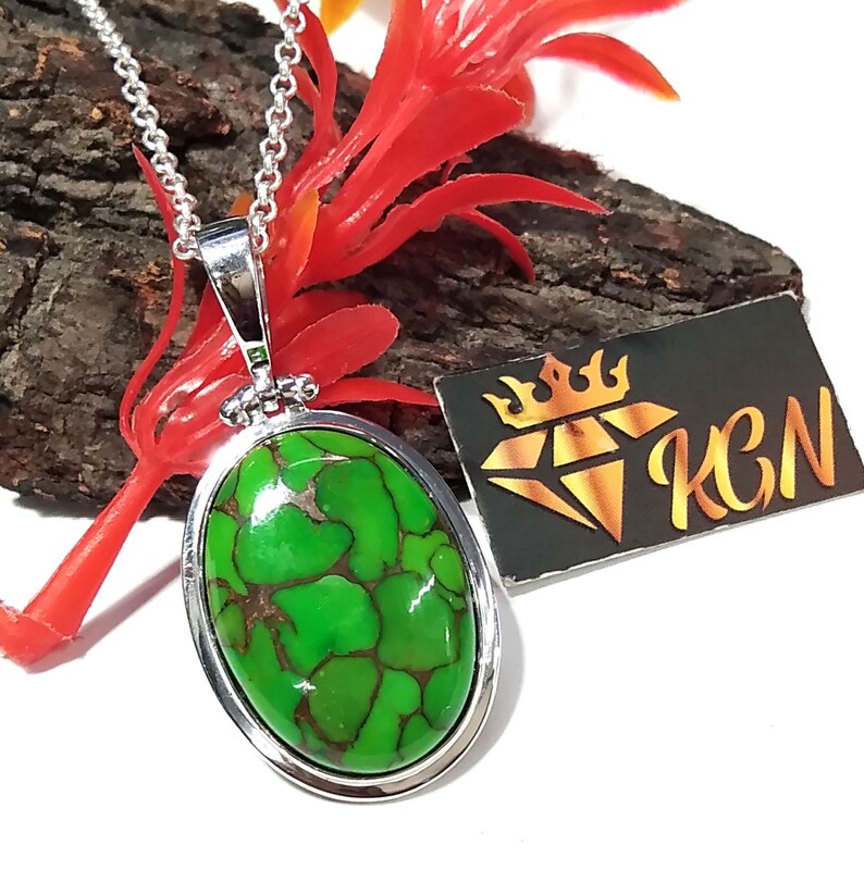 Puede incluir: Un collar de cadena de plata con un colgante ovalado con una piedra turquesa verde y marr&oacute;n. El colgante tiene un borde de plata.