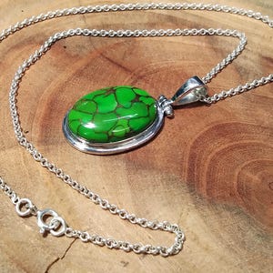 Puede incluir: Un collar de cadena de plata con un colgante ovalado verde con una piedra turquesa. La piedra tiene un patr&oacute;n de m&aacute;rmol.