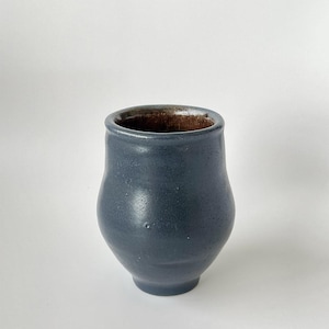 May include: A dark blue ceramic cup with a rounded bottom and a slightly flared rim. The cup has a speckled glaze and a brown interior.