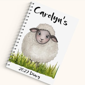 May include: A spiral-bound diary with a white cover featuring a cartoon illustration of a fluffy sheep standing in green grass. The text Carolyn's is printed in black above the sheep, and the text 2027 Diary is printed in black below the grass.
