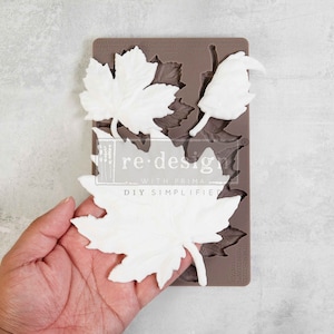 Może przedstawiać: Brązowa silikonowa forma z nadrukiem "re.design with prima DIY SIMPLIFIED" i "FALLING LEAVES FANTASY". Forma zawiera kilka kształtów liści, w tym liście klonowe i pojedynczy kwiat.
