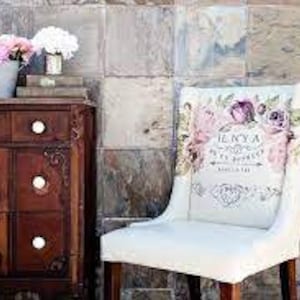 Può includere: Una sedia imbottita bianca con uno schienale a motivi floreali. Il motivo floreale comprende rose rosa, viola e verdi. La sedia ha una struttura e gambe in legno.