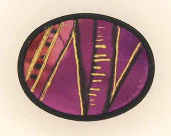 Two silk brooches, black border with graphic pattern, semicircular brooch with gold border, small landscape.