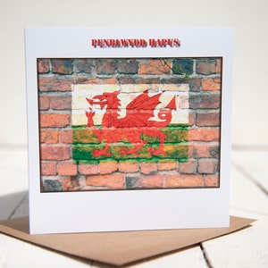May include: A white card with a red brick background featuring the Welsh flag with a red dragon. The text "PENBLWYDD HAPUS" is printed in red at the top of the card.