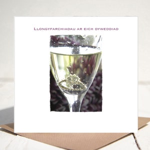 May include: A wedding card with a champagne flute and a wedding ring inside. The card reads "Llongyfarchiadau ar Eich Dyweddiad" which translates to "Congratulations on your wedding" in Welsh.