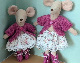 Könnte beinhalten: Zwei Stoffmauspuppen. Jede Maus trägt eine rosa Strickjacke, einen Rock mit Blumendruck und Spitzenbesatz sowie rosa Ballettschuhe, die mit weißen Bändern gebunden sind. Die Mäuse haben große, beige Ohren und braune Nasen.