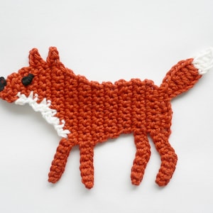 Könnte beinhalten: Eine gehäkelte Fuchs-Applikation in Orange und Weiß. Der Fuchs hat eine schwarze Nase und Augen.