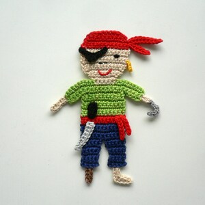 Könnte beinhalten: Gehäkelte Piratenfigur mit rotem Bandana, grünem Hemd, blauer Hose und schwarzem Augenklappen. Die Figur hält ein weißes Messer und hat einen grauen Haken als Hand.
