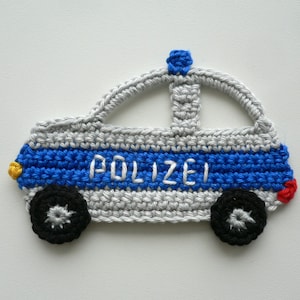 Könnte beinhalten: Ein gehäkeltes Polizeiauto in Grau, Blau, Rot und Gelb mit dem Wort "Polizei" in Weiß an der Seite.