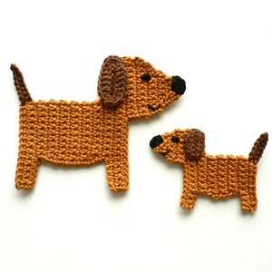 Könnte beinhalten: Zwei gehäkelte Hunde-Applikationen. Die Hunde sind braun mit dunkelbraunen Ohren, Schwänzen und schwarzen Nasen. Der größere Hund ist etwa 13 cm hoch, der kleinere Hund etwa 8 cm. Die Hunde befinden sich auf weißem Hintergrund.