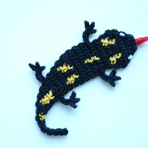 Könnte beinhalten: Ein schwarzer und gelber gehäkelter Salamander mit roter Zunge. Der Salamander ist ein flaches, zweidimensionales Design.