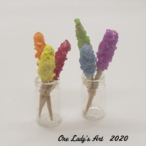 May include: Two clear glass jars filled with colorful candy sticks. The candy sticks are red, yellow, orange, green, and purple. The jars are on a white background.