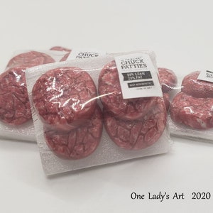 May include: Several packages of raw chuck patties, wrapped in clear plastic. Each package has a label that reads "CHUCK PATTIES" with the text "80% LEAN 20% FAT". The patties are red and appear fresh.