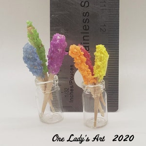 May include: Two glass jars filled with colorful rock candy on sticks. The jars are clear and the candy is red, orange, yellow, green, and blue.
