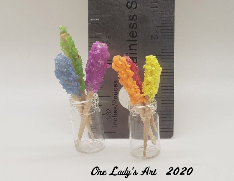 May include: Two glass jars filled with colorful rock candy on sticks. The jars are clear and the candy is red, orange, yellow, green, and blue.