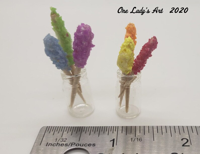 May include: Two glass jars filled with colorful candy sticks on wooden skewers. The jars are about 1 inch tall and are sitting on a ruler. The ruler is marked in inches and 1/16ths of an inch. The text "One Lady's Art 2020" is visible in the top right corner of the image.