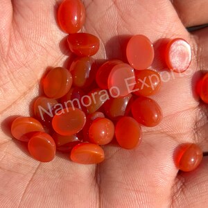 K&ouml;nnte beinhalten: Eine Sammlung von 20 ovalen Karneol-Edelsteinen. Die Steine sind tief orange-rot und haben eine glatte, polierte Oberfl&auml;che.