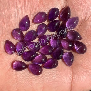 以下が含まれることがあります： 25個の紫色のアメジストの洋梨型のカボションのセット。石は滑らかで磨かれており、深い紫の色合いをしています。