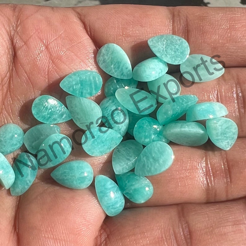 May include: A collection of teal green gemstone cabochons in a pear shape. The stones are smooth and polished, with a translucent appearance.